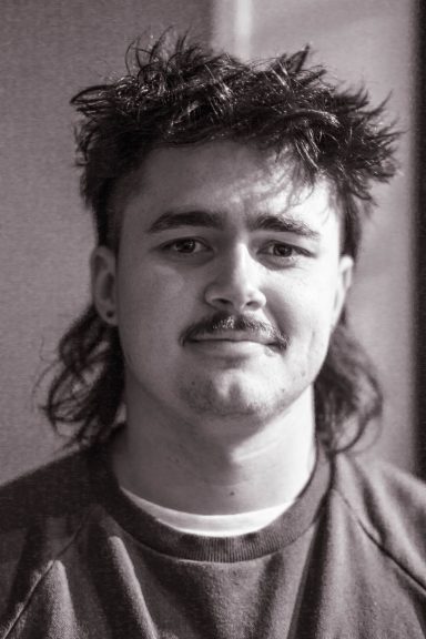 En man med frisyr med bakhuvud och mustasch, klädd i en sweatshirt.