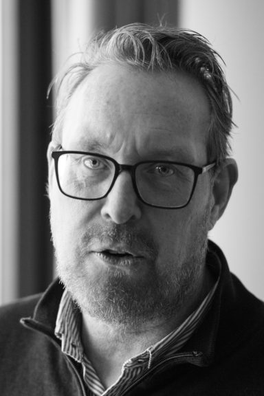 Porträtt av en man med glasögon och skägg, som ser direkt in i kameran.