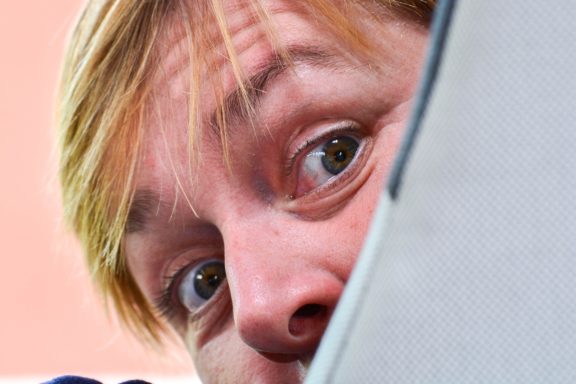 Närbild av en person som kollar fram bakom en grå yta med ett nyfiket uttryck.