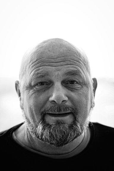 Porträtt av en skäggig man med kort, skallig frisyr, leende mot kameran.